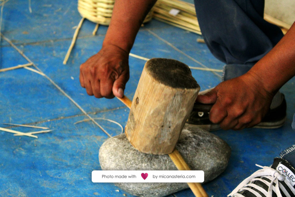 Artesano golpeando con un mazo de madera una tira de carrizo.